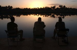 Three men sitting, facing a lake.
