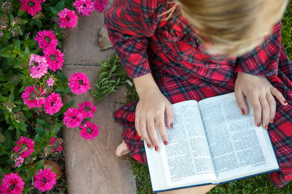 A young girl sits in a garden and reads the Book of Mormon. via lds.org © intellectual reserve